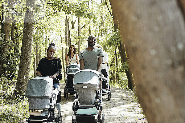 Freunde unterhalten sich beim Spaziergang mit Kinderwagen auf dem Fußweg im Park