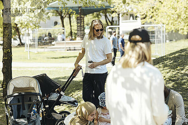 Mann mit Kinderwagen im Gespräch mit Freunden im Park