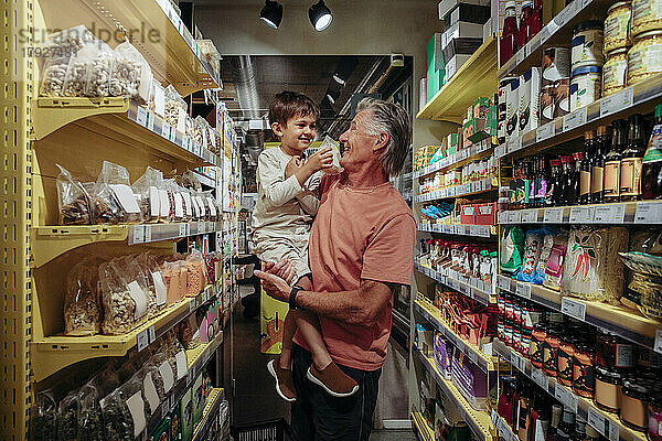 Lächelnder älterer Mann mit Enkel beim Einkaufen von Snacks im Supermarkt
