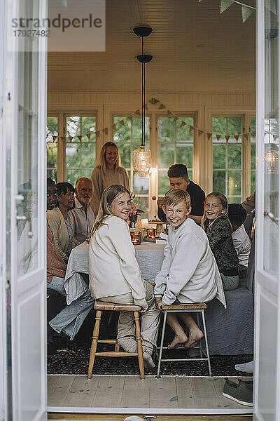 Junge und Mädchen schauen über die Schulter  während sie auf einem Hocker am Esstisch mit ihrer Familie sitzen