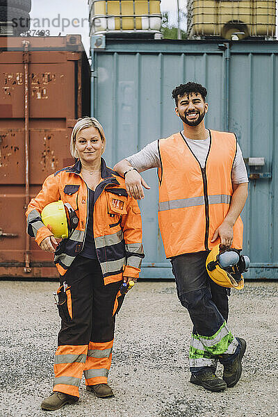 Lächelnde männliche und weibliche Bauarbeiter in reflektierender Kleidung auf der Baustelle in voller Länge