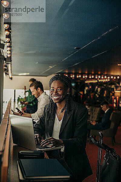 Porträt einer lächelnden Unternehmerin  die mit einem Laptop in einer Hotelhalle sitzt