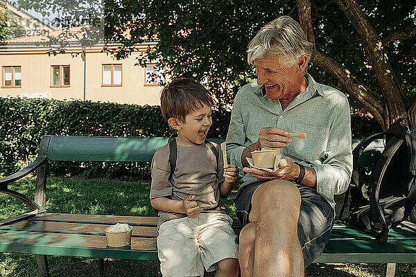 Glücklicher Großvater und Enkel genießen auf einer Bank sitzend Eiscreme