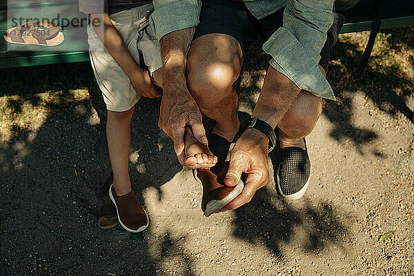 Hohe Winkel Ansicht des Mannes hilft Enkel tragen Schuh auf sonnigen Tag