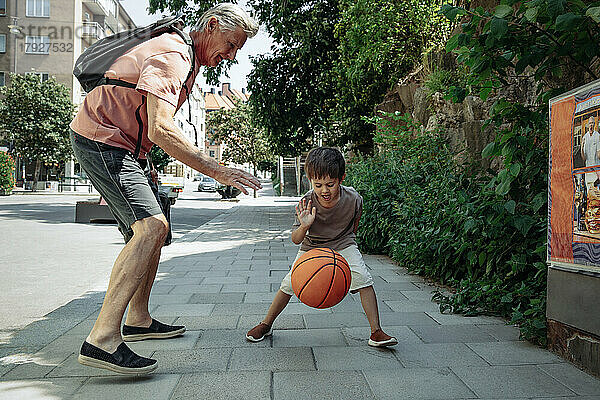 Großvater spielt Basketball mit Enkel auf dem Bürgersteig
