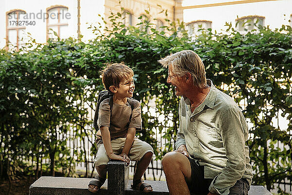 Enkel im Gespräch mit Großvater auf der Bank sitzend