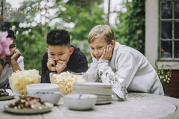 Neugierige Jungen stützen sich auf die Ellbogen und betrachten eine Schüssel mit Snacks auf dem Tisch