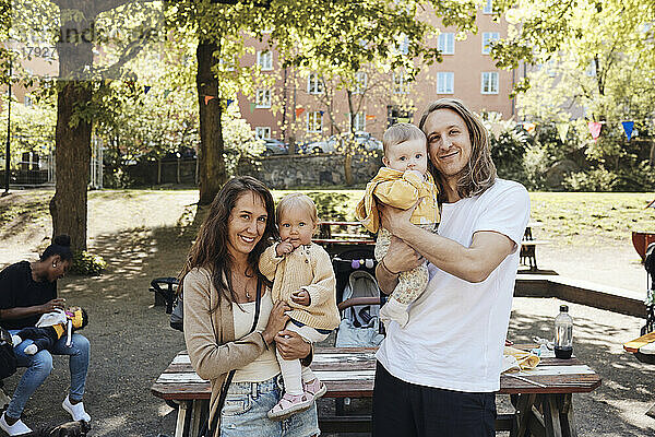 Porträt von lächelnden Eltern  die ihre Töchter in den Kindergarten tragen