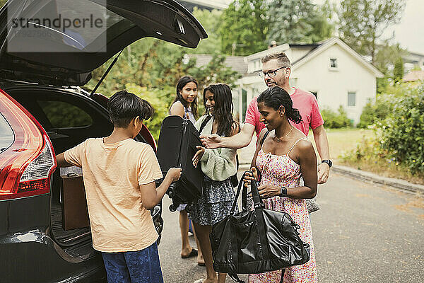 Eine gemischtrassige Familie entlädt ihr Gepäck aus dem Kofferraum  während sie auf der Straße steht