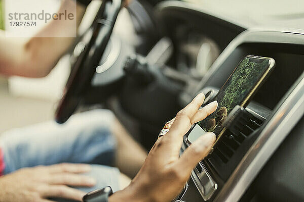 Hand einer Frau  die das GPS über ein am Armaturenbrett im Auto befestigtes Smartphone benutzt