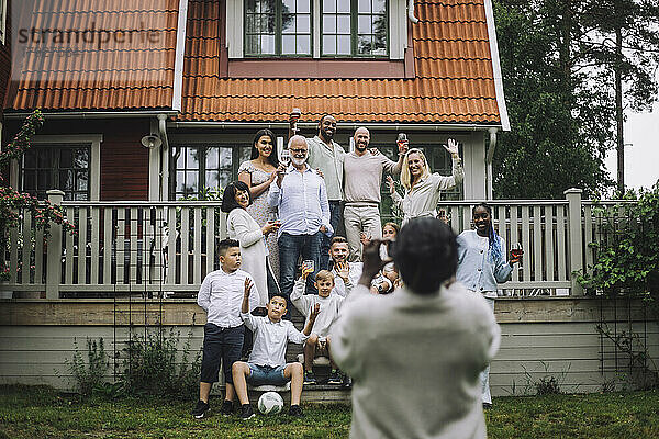 Frau fotografiert fröhliche Mehrgenerationenfamilie auf der Veranda vor dem Haus