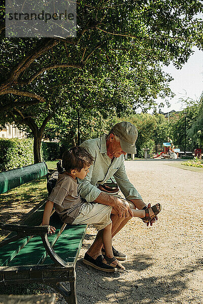Großvater hilft seinem Enkel  der eine Sandale trägt  während er auf einer Bank im Park sitzt
