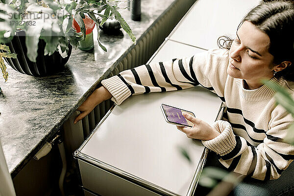 Hochformatige Ansicht einer Frau  die die Temperatur eines Heizkörpers über eine Smartphone-Anwendung zu Hause überprüft