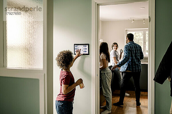 Seitenansicht eines Jungen  der eine Smart-Home-App auf einem digitalen Tablet benutzt  während die Familie in der Küche steht