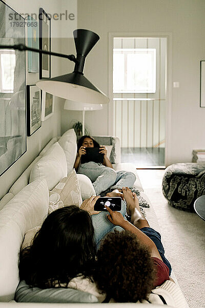 Familie nutzt drahtlose Technologien  während sie zu Hause auf dem Sofa liegt