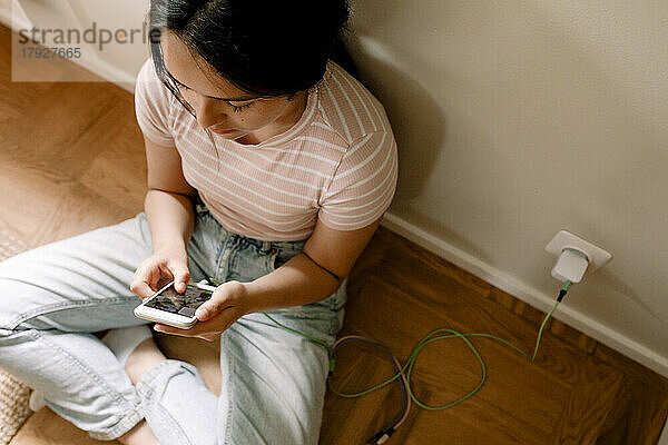 High-Winkel-Ansicht des Mädchens mit Smartphone beim Sitzen an der Wand zu Hause