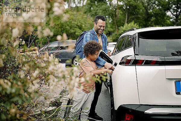 Lächelnder Mann mit Sohn lädt Elektroauto