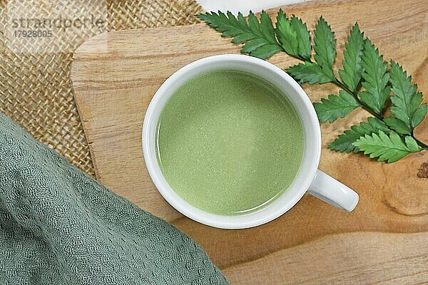 Draufsicht auf eine Tasse grünen Tee Latte auf einem Holzbrett