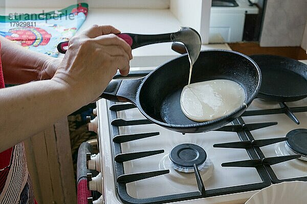 Der Teig breitet sich in einer Pfanne zum Backen von Pfannkuchen in den Händen einer älteren Frau aus