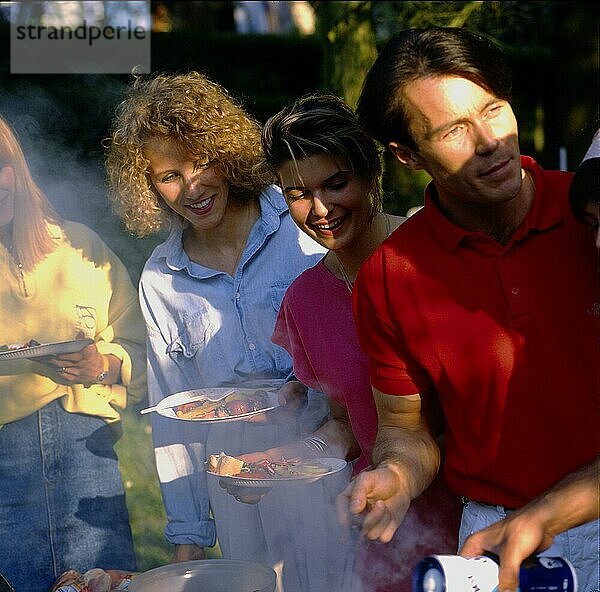 Gartenparty junge Leute beim Essen  Grillen  Grillparty  3 Personen  Frauen und Männer  Teller in der Hand  auf das Grillgut schauend