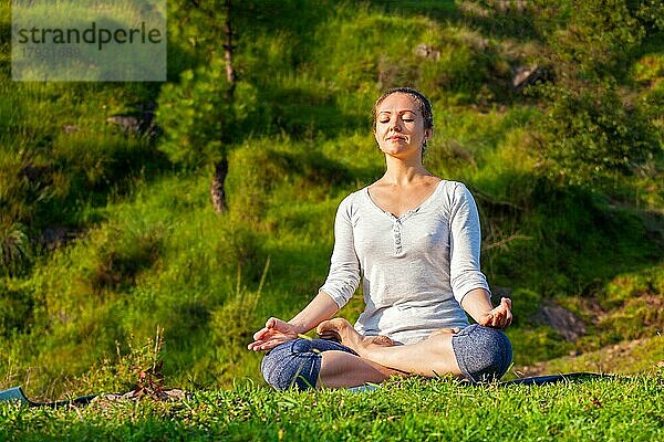 Junge sportliche Frau macht Yoga im Freien  meditiert und entspannt sich in Padmasana Lotus Pose) mit Kinn Mudra auf grünem Gras im Wald