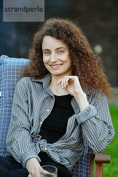 Porträt einer lächelnden jungen Frau mit langen lockigen Haaren im Freien