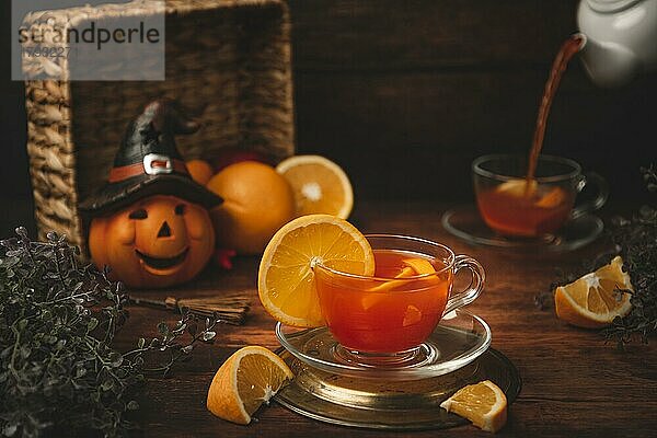 Tee mit Orange in Tasse  auf hölzernen Untergrund  vor Halloweendekoration