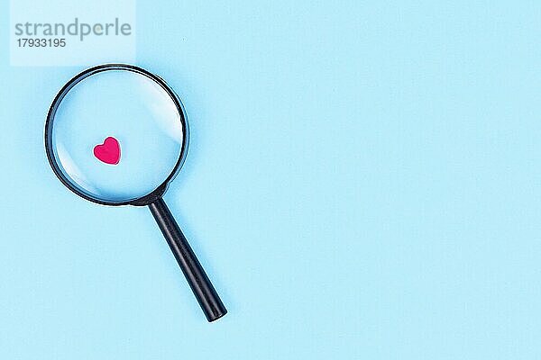Auf der Suche nach Liebe Konzept mit Lupe Glas und rosa Herz Symbol auf blauem Hintergrund mit Kopie Raum