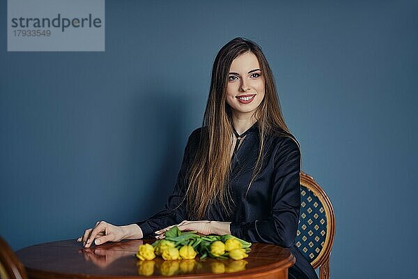 Schöne junge Frau sitzt hinter dem Tisch mit Tulpen