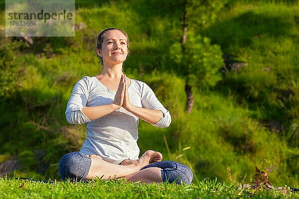 Meditation und Entspannung Yoga im Freien  junge Frau meditiert und entspannt in Padmasana Lotus Pose mit Namaste Anjali Mudra auf grünem Gras im Wald