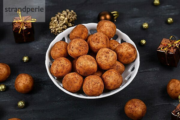 Traditionelle deutsche Weihnachtsbonbons  genannt Marzipankartoffeln. Runde  kugelförmige Marzipankartoffeln mit Zimt und Kakaopulver in einer weißen Schale auf dunklem Hintergrund