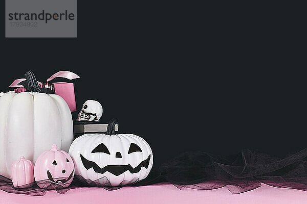 Rosa und weiße Halloween-Dekoration mit schwarzen und weißen Kürbissen  Zauberbücher und Spinnen auf schwarzem Hintergrund mit Kopierraum