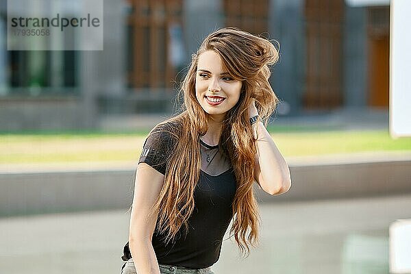 Positive und glückliche junge Frau mit langen lockigen Haaren im Freien