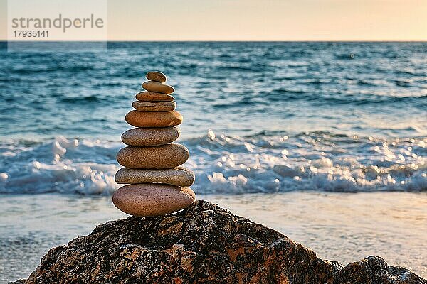 Konzept des Gleichgewichts und der Harmonie. Cairn Stapel von Steinen Kieselsteine Steinhaufen am Strand Küste des Meeres in der Natur auf Sonnenuntergang. Meditative Kunst des Steinstapelns