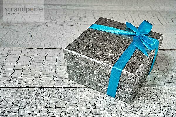 Geschenk Geburtstag Weihnachtsgeschenk Konzept  silberne Geschenk-Box mit blauem Band auf weiß lackiertem Holz Hintergrund. Ansicht von oben