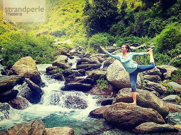 Yoga im Freien  Frau macht Yoga-Asana Natarajasana  Herr des Tanzes Gleichgewichtspose im Freien am Wasserfall im Himalaya. Vintage Retro-Effekt gefiltert Hipster-Stil Bild
