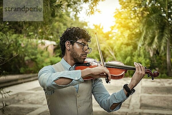 Porträt eines Geige spielenden Mannes bei Sonnenuntergang. Nahaufnahme von Geiger Mann spielt auf der Straße. Violinist Künstler spielt eine Melodie im Freien  Bild einer Person spielt die Geige im Freien