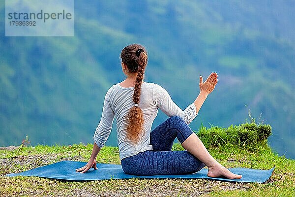 Hatha Yoga im Freien  sportlich fitte Frau bei der Yoga-Asana Parivrtta Marichyasana (oder Ardha Matsyendrasana)  sitzende Wirbelsäulendrehung im Freien in den Bergen
