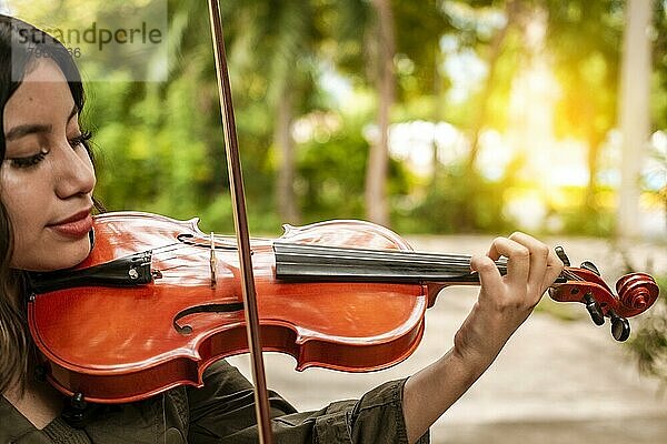 Nahaufnahme eines Mädchens mit ihrer Geige  das im Freien eine Melodie spielt  Konzept einer lächelnden Geigerin. Attraktives Mädchen spielt Geige im Freien. Porträt eines Geige spielenden Mädchens im Freien