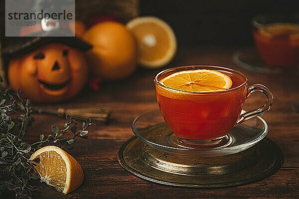 Tee mit Orange in Tasse  auf hölzernen Untergrund  vor Halloweendekoration