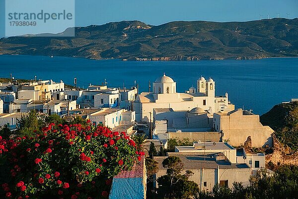 Blick auf das Dorf Plaka auf der Insel Milos über rote Geranienblüten bei Sonnenuntergang. Plaka Stadt  Insel Milos  Griechenland. . Fokus auf Blumen