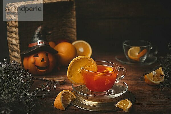 Tee mit Orange in Tasse  auf hölzernen Untergrund  vor Halloweendekoration