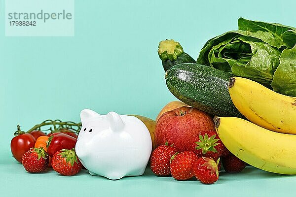 Konzept für Kosten für gesunde Ernährung oder Geld sparen beim Kauf von Lebensmitteln. Gemüse und Früchte neben einem Sparschwein auf blauem Hintergrund mit Kopierraum