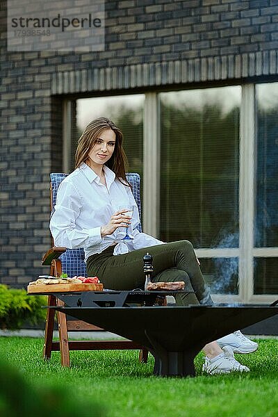 Nette junge Frau sitzt auf einem Stuhl mit einem Glas Limonade im Hinterhof