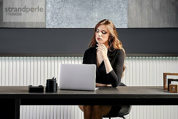 Junge Frau  die im Büro hinter dem Schreibtisch sitzend auf die Verbindung eines Online-Anrufs wartet