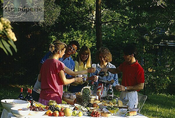 Gartenparty  Essen und Trinken  reich gedeckter Tisch  Obst  Gemüse  Früchte  Brot  Käse  Wein Teller  Schüsseln  junge Leute  3 Frauen  2 Männer  5 Personen  Anstoßen  Picknick  Essen im Freien