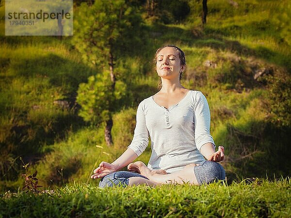 Junge sportlich fitte Frau macht Yoga im Freien  meditiert und entspannt in Padmasana Lotus Pose) mit Kinn Mudra auf grünem Gras im Wald. Vintage Retro-Effekt gefiltert Hipster-Stil Bild