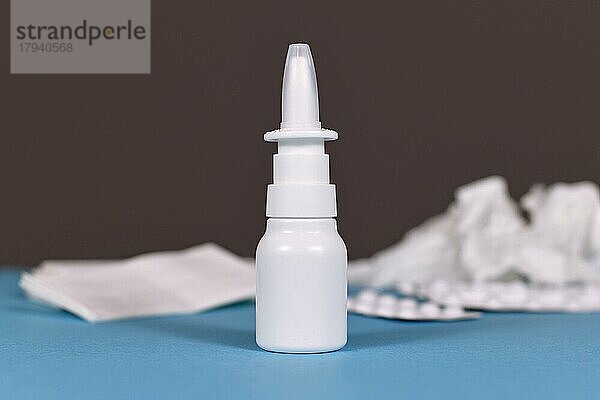Nasensprayflasche mit zerknüllten Tüchern und Tabletten gegen Erkältung im unscharfen Hintergrund