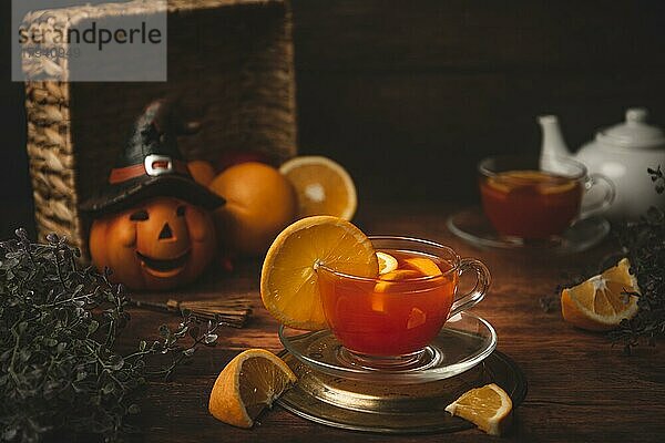 Tee mit Orange in Tasse  auf hölzernen Untergrund  vor Halloweendekoration