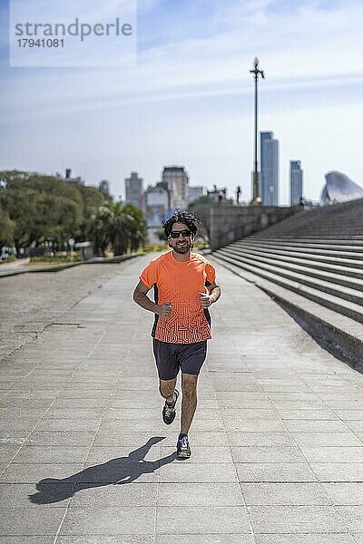 Porträt von gut aussehend attraktiv reifen bärtigen sportlichen lateinischen Mann Kerl 40s in orange T-Shirt läuft auf der Straße